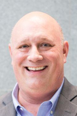 a man wearing a suit and tie smiling at the camera