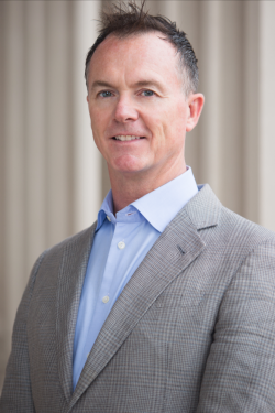 a man wearing a suit and tie smiling at the camera