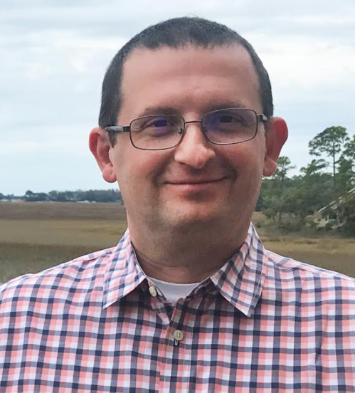 a man wearing glasses and smiling at the camera